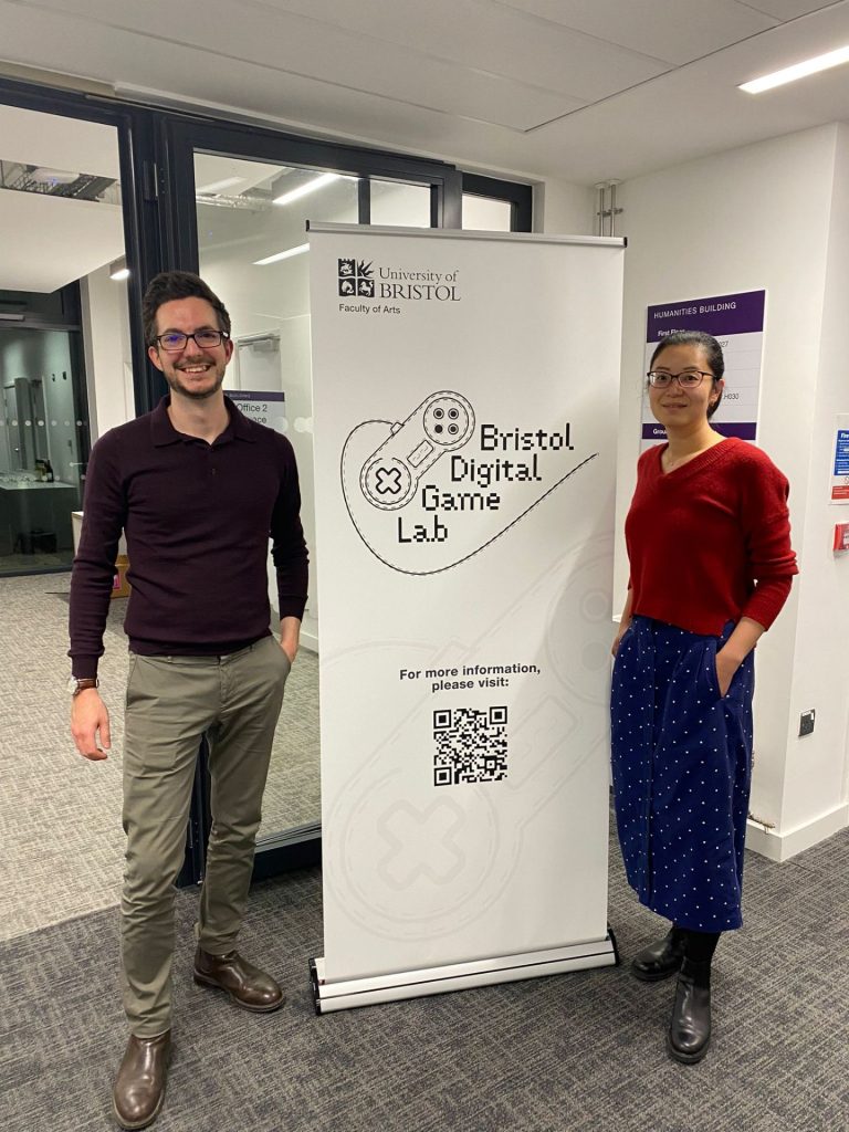 Two people beside a roller banner for the Bristol Digital Game Lab
